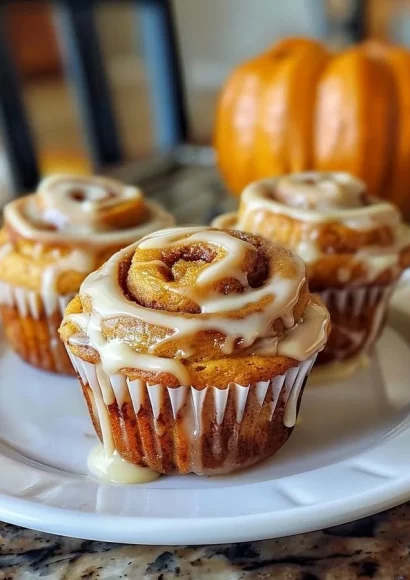 Delicious pumpkin cinnamon roll muffins topped with creamy icing on a plate